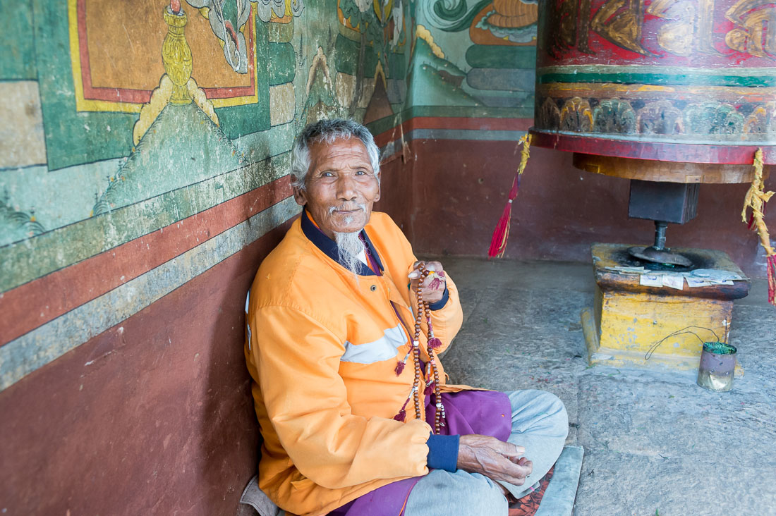 Old man at Punakha Dzong monastery  praying using the Buddhist malas (prayer beads) while performing the ritual spinning of the praying wheel, Kingdom of Bhutan, Asia