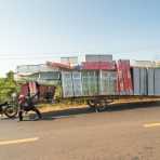 A really large and long trailer fully loaded with aluminum cabinet displays and mattresess, being towed by a small motorcycle. Kingdom of Cambodia, Indochina, South East Asia
