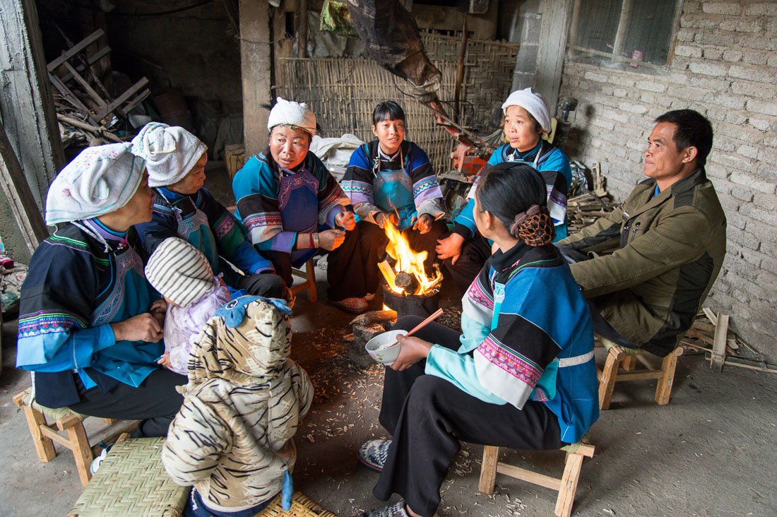 Women from the Bu Yi ethnic minority people, in traditional costume, gathering next to the fire, eating sunflower seeds. La Zhe village, Luo Ping County, Yunnan Province, China, Asia. Nikon D4, 24-120mm, f/4.0, VR