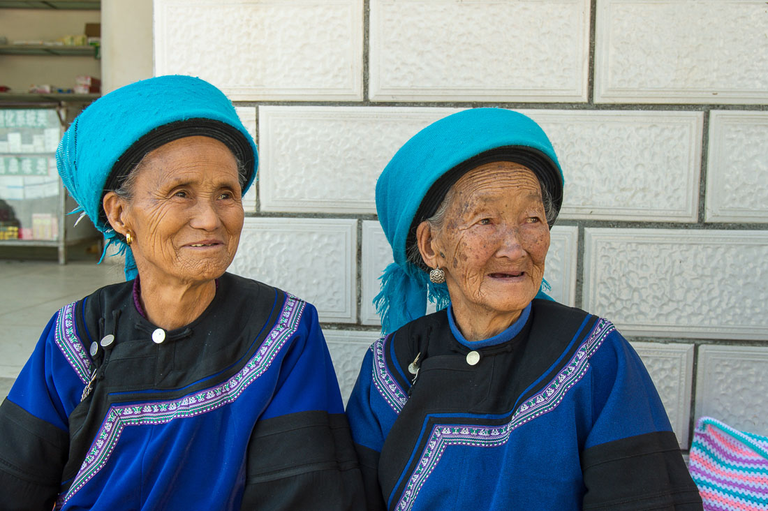 Two joyful old women from the Yi ethnic minority people in their traditional costumes at the market in Jia Yin village. Yunnan Province, China, Asia. Nikon D4, 24-120mm, f/4.0, VR