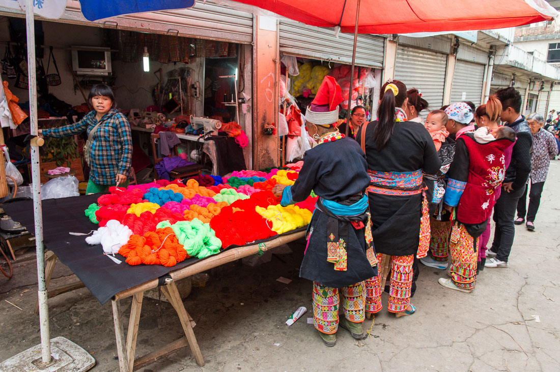 Women from the Yao ethnic minority people wearing the traditional costume at Jin Ping market buying colorful cotton yarn. Jin Ping County, Yunnan Province, China, Asia. Nikon D4, 24-120mm, f/4.0, VR