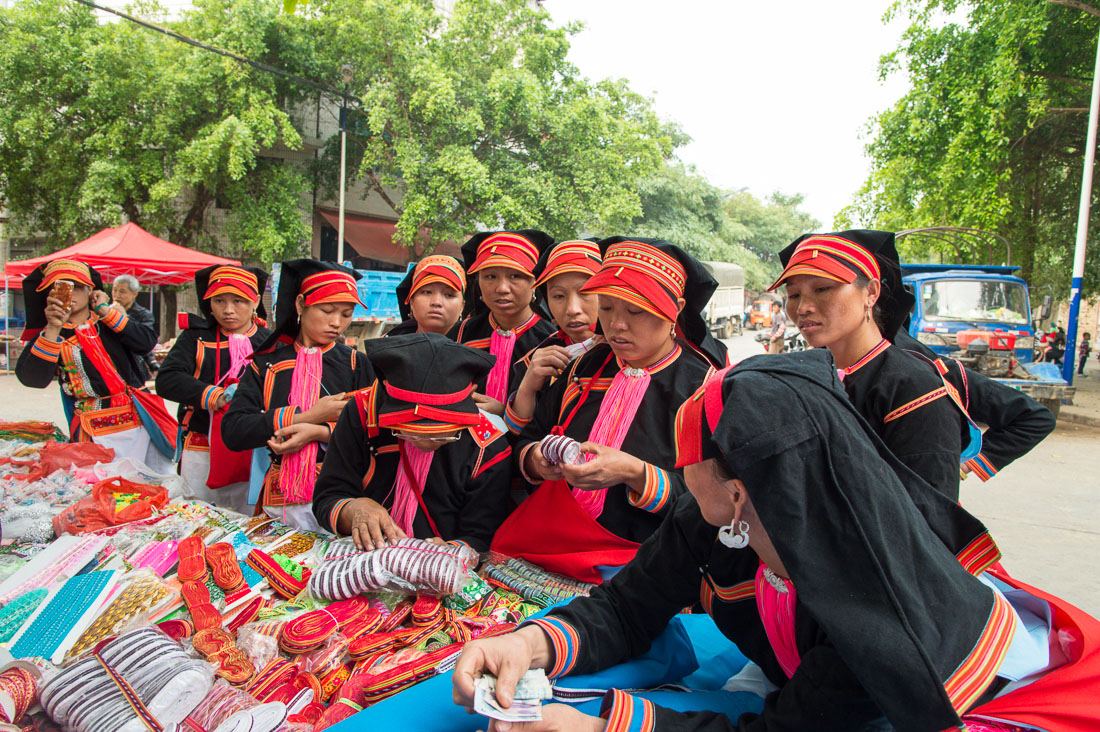 A group of women from the Yao ethnic minority people wearing the traditional costume at Jin Shui He market buying colorful trimming. Jin Ping County, Yunnan Province, China, Asia. Nikon D4, 24-120mm, f/4.0, VR