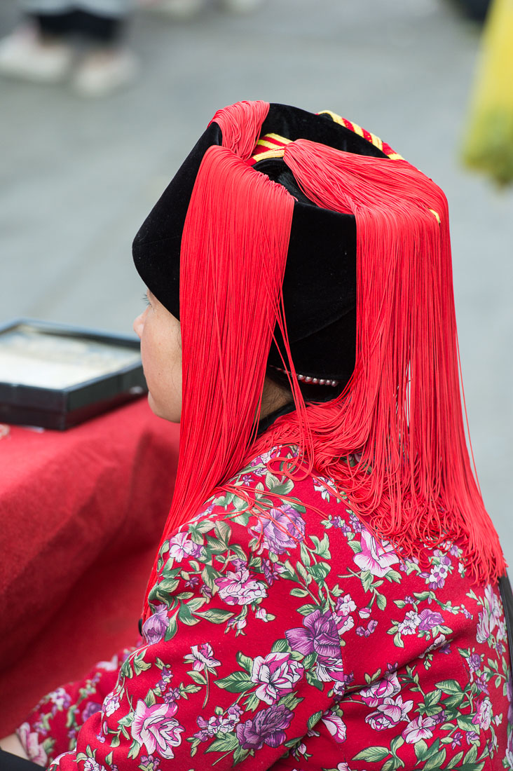 Colorful and unusual hat worn by the women from the Ha Ni ethnic minority people. Ping He market,, Lu Chun County, Yunnan Province, China, Asia. Nikon D4, 70-200mm, f/2.8, VR II