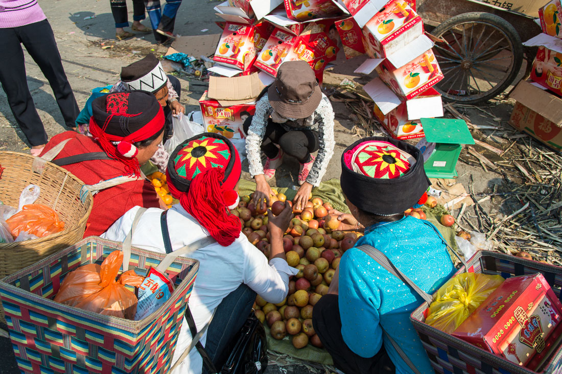 Women from the Ha Ni ethnic minority people in traditional costumes, buying apples at the Ping He market, Lu Chun County, Yunnan Province, China, Asia. Nikon D4, 24-120mm, f/4.0, VR