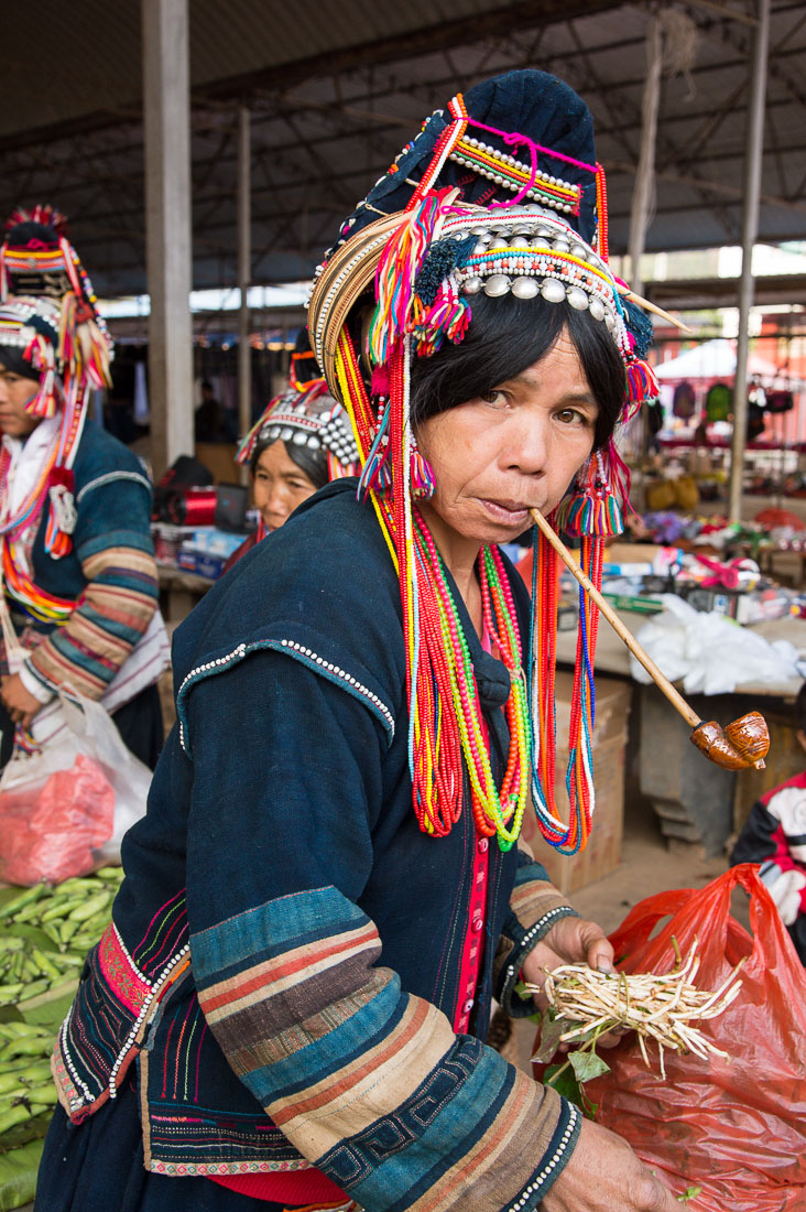 Woman from the Ha Ni ethnic minority people in colorful costume, smoking the traditional pipe. Mang Xin market, Meng Lian County, Yunnan Province, China, Asia. Nikon D4, 24-120mm, f/4.0, VR
