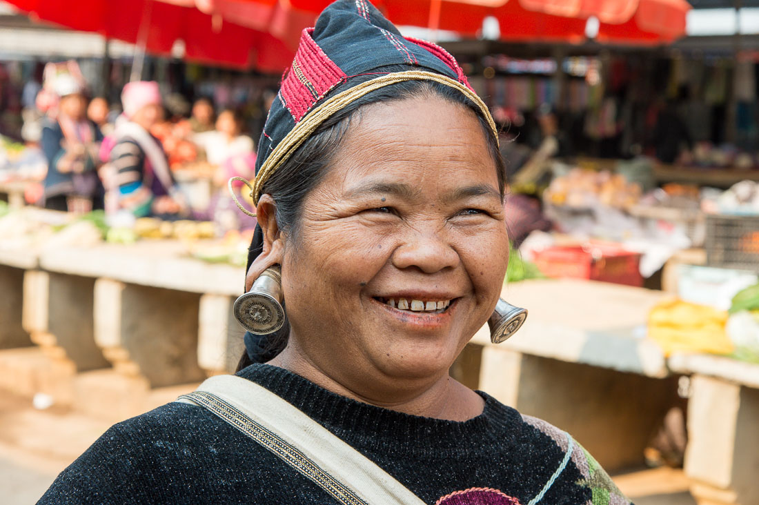 A joyful woman from the Bulang ethnic minority people wearing the unique traditional earring. Mang Xin market, Meng Lian County, Yunnan Province, China, Asia. Nikon D4, 70-200mm, f/2.8, VR II