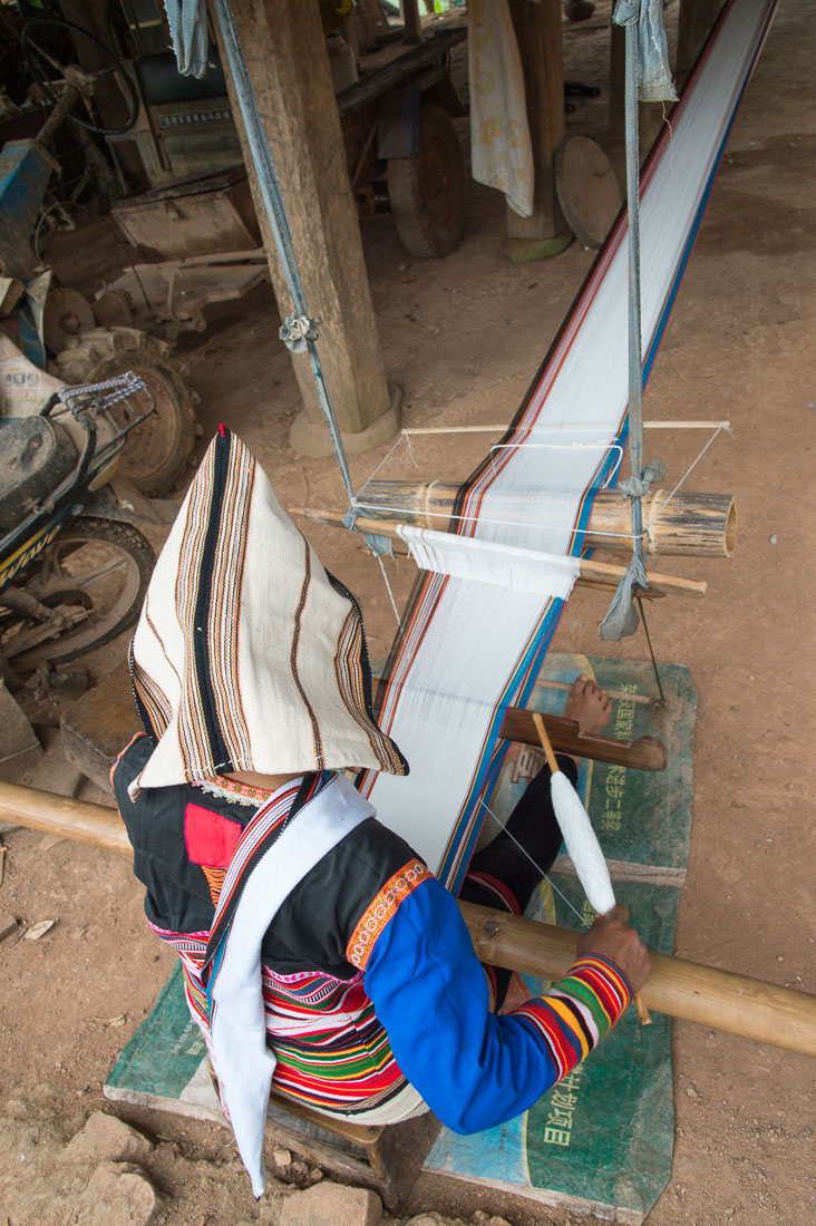 A woman from the Ji Nuo ethnic minority people, in traditional costume, weaving on the old family loom. Ba Sa Lao Zhai village, Xi Shuang Ban Na prefecture, Yunnan province, China, Asia. Nikon D4, 24-120mm, f/4.0, VR