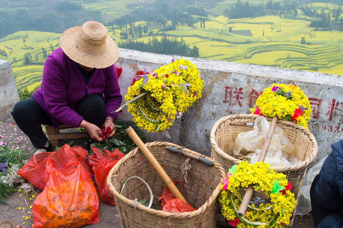 Han Chinese woman making wreaths from rapeseed flowers for Chinese tourists. Luo Ping County, Yunnan Province, China, Asia. Nikon D4, 24-120mm, f/4.0, VR