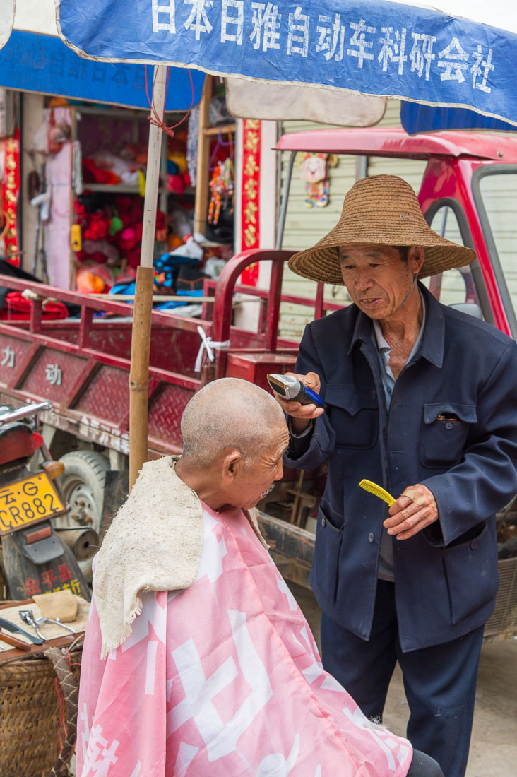 Skilled barber with electric razor attending a customer. Jin Ping market, Yunnan Province, China, Asia. Nikon D4, 24-120mm, f/4.0, VR