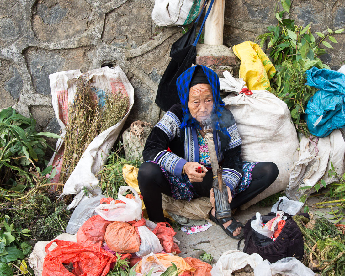 An old woman from the Miao ethnic minority people, smoking a bong handmade from plastic bottles. She sells medicinal herbs at the Jin Ping market. Yunnan Province, China, Asia. Nikon D4, 24-120mm, f/4.0, VR