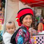 A joyful mother from the Ha Ni ethnic minority people carrying her baby, wearing traditional costume at the Ping Hi town market, Lv Chun county, Yunnan Procince, China, Asia. Nikon D4, 24-120mm, f/ 4.0, VR.