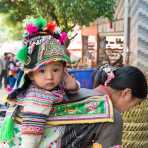 A mother from the Yi ethnic minority people carrying her baby, wearing traditional costume at the Lai Ji Zhai town market, Yunnan Procince, China, Asia. Nikon D4, 24-120mm, f/ 4.0, VR.