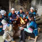 Women from the Bu Yi ethnic minority people, in traditional costume, gathering next to the fire, eating sunflower seeds. La Zhe village, Luo Ping County, Yunnan Province, China, Asia. Nikon D4, 24-120mm, f/4.0, VR