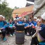 Women from the Bu Yi ethnic minority people, in traditional costume, attending a funeral, gathering next to a cooking fire, eating sunflower seeds. La Zhe village, Luo Ping County, Yunnan Province, China, Asia. Nikon D4, 24-120mm, f/4.0, VR