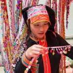 Young woman from the Yao ethnic minority people wearing the traditional costume at Jin Shui He market buying colorful ornaments. Jin Ping County, Yunnan Province, China, Asia. Nikon D4, 70-200mm, f/2.8, VR II