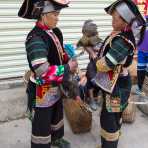 Two women from the Yi ethnic minority people in traditional costumes exchanging comments on newly purchased poultry. Lao Ji Zhai market, Yunnan Province, China, Asia. Nikon D4, 24-120mm, f/4.0, VR