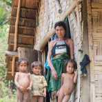 A woman from the Kuy people ethnic minority wearing the traditional costume, with children on the porch of her bamboo home, Meung Ngeun district. Lao PDR, Indochina, South East Asia