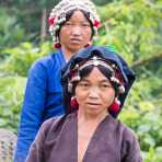 Two women from the Akha people ethnic minority wearing the traditional and elaborate hat, Luang Namtha Province. Lao PDR, Indochina, South East Asia