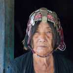 Old woman from the Akha Korpean people ethnic minority wearing her traditional costume and elaborate hat, at her house door. Phicheu Mai village, Bokeo province, Lao PDR, Indochina, South East Asia.