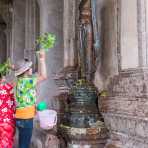 Worshipers sprinkling Buddha statues using little branch with leaves during the Lao new year celebration, Vientiane. Lao PDR, Laos, Indochina, South East Asia