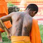 Buddhist monk with religious tattos on his back, gardening around Wat Tat Luang, Vientiane, Lao PDR, Indochina, South East Asia.