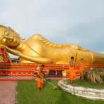 Buddhist monks gardening in front of a colossal statue of reclining Buddha at Wat Tat Luang Neua, Vientiane, Lao PDR, Indochina, South East Asia.