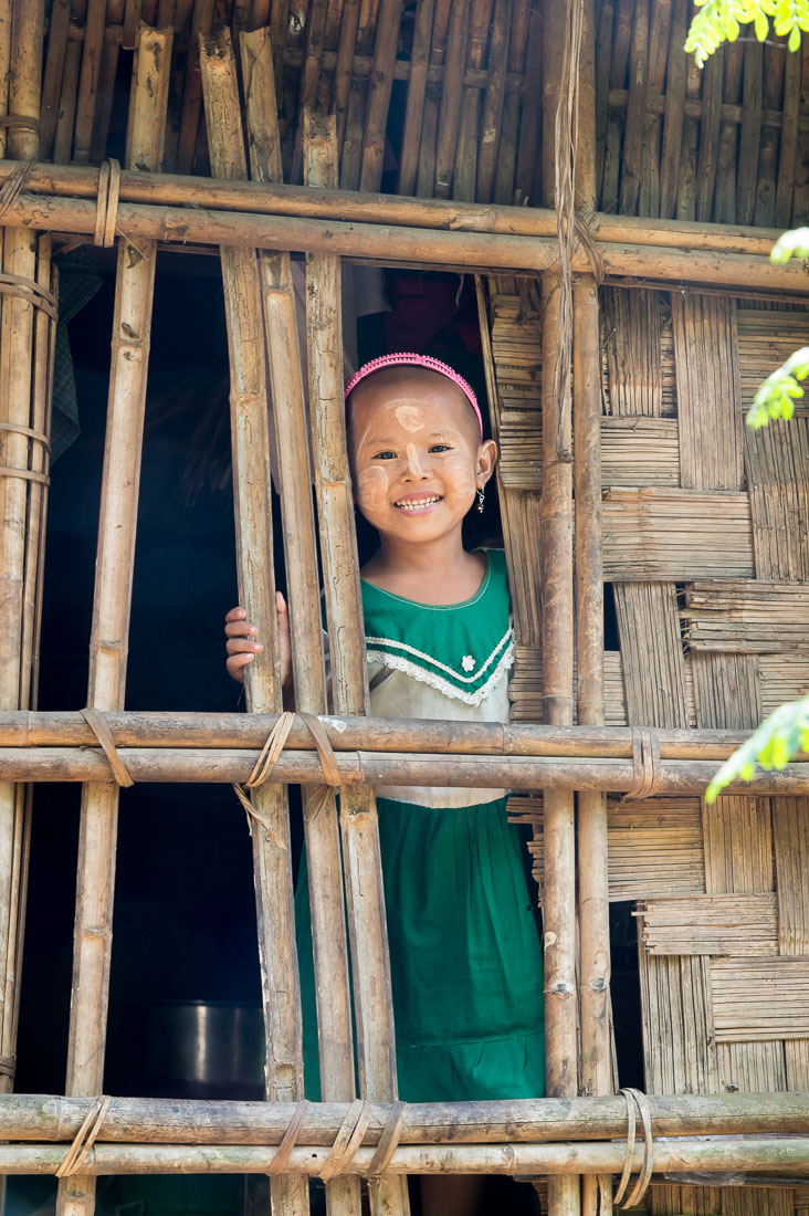 Little girl looking out from the window of her bamboo house, her face with patches of Tha Nat Khar an extract from tree roots commonly used to protect the skin from the sun. Chin Village, Rakhine State, Myanmar, Indochina, South East Asia.