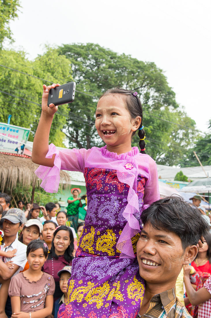 Smiling and happy little girl on her father shoulders taking pictures of the parade. Manhua Village, Myanmar, Indochina, South East Asia