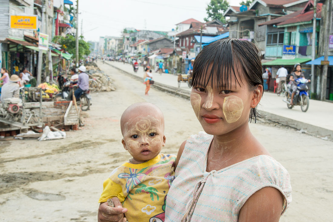 Young mother carrying her baby, both  with the faces covered by white patches of Tha Nat Khar , an extract from the tree roots used by the Burmese people to protect the skin from the sun. Sittwe, Rakhine State, Myanmar, Indochina, South East Asia
