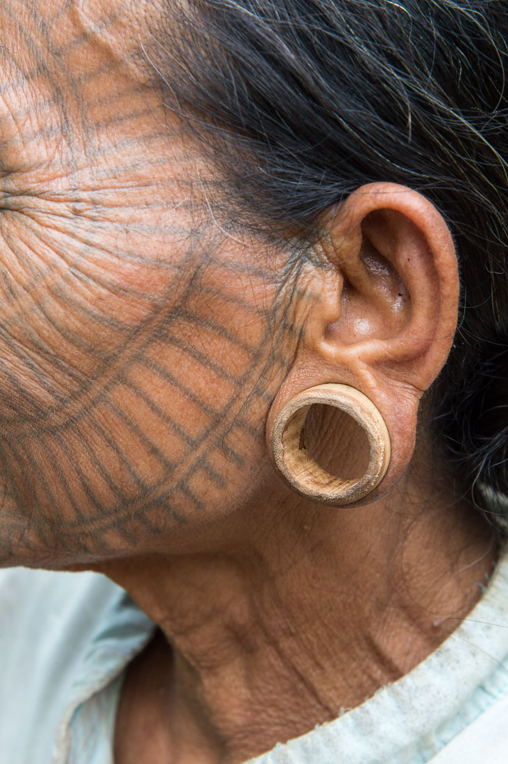 Old woman with the face full covered from spider web tattos, a mysterious and old tradition which was practiced until 60 years ago. There are 7 villages on the Lamro river with about 20 old women left with spider web tattoos on their face, all aged more than 65 years. Particular of her bamboo earring once in silver, but all sold in the yeras. Chin Village, Rakhine State, Myanmar, Indochina, South East Asia.