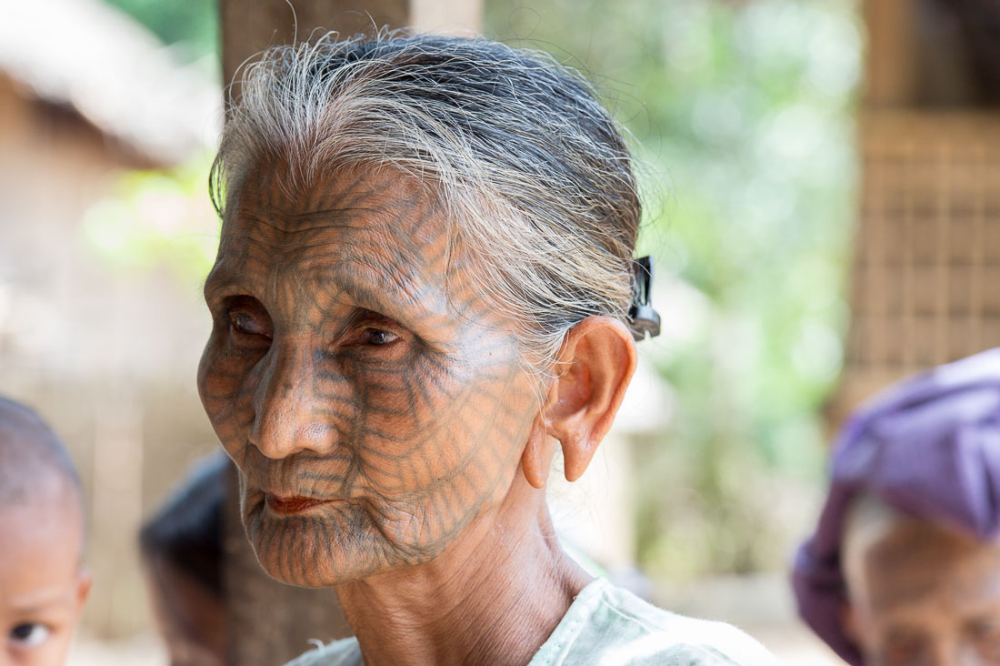 Old woman with the face full covered from spider web tattos, a mysterious and old tradition which was practiced until 60 years ago. There are 7 villages on the Lamro river with about 20 old women left with spider web tattoos on their face, all aged more than 65 years. Chin Village, Rakhine State, Myanmar, Indochina, South East Asia.