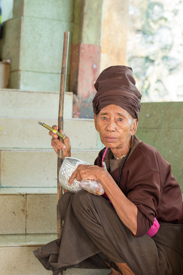 Old beggar smoking a cigar on the stairs of the Buddhist religious site of Mount Popa, Myanmar, Indochina, South East Asia.