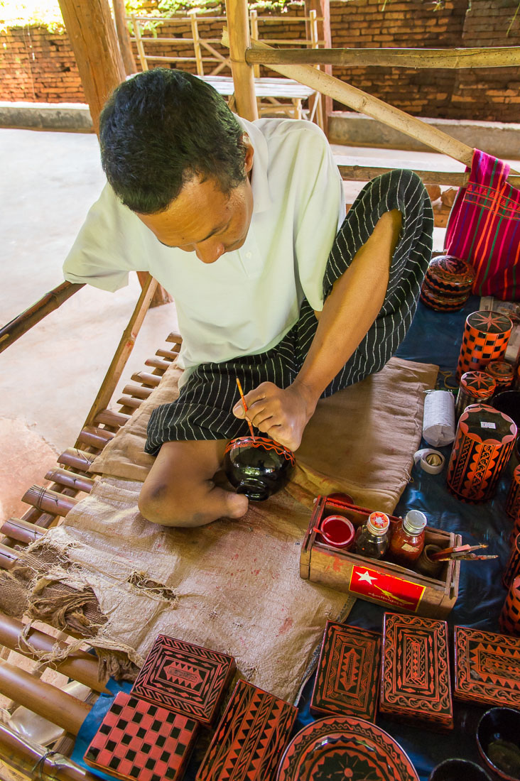 A disabled person and talented artist, born with one limb only, his left leg and foot,  detailing a bamboo lacquer bowl using a small brush with his foot. Shwe Indein pagoda, Indein Village, Inle lake, Shan State, Mynamar, Indochina, South East Asia.