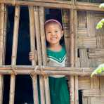 Little girl looking out from the window of her bamboo house, her face with patches of Tha Nat Khar an extract from tree roots commonly used to protect the skin from the sun. Chin Village, Rakhine State, Myanmar, Indochina, South East Asia.