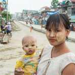 Young mother carrying her baby, both  with the faces covered by white patches of Tha Nat Khar , an extract from the tree roots used by the Burmese people to protect the skin from the sun. Sittwe, Rakhine State, Myanmar, Indochina, South East Asia