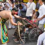 Psychic medium follower of the Bang New Shrine, with long needles pierced through his ears, offering spiritual blessing to a sick woman in a wheel chair, during a street procession in the annual Chinese vegetarian festival. Phuket, Kingdom of Thailand, Indochina, South East Asia