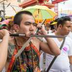 Psychic medium follower of the Bang New Shrine, with two large oriental knives blades pierced through his cheecks, taking part in a street procession during the annual Chinese vegetarian festival. Phuket, Kingdom of Thailand, Indochina, South East Asia