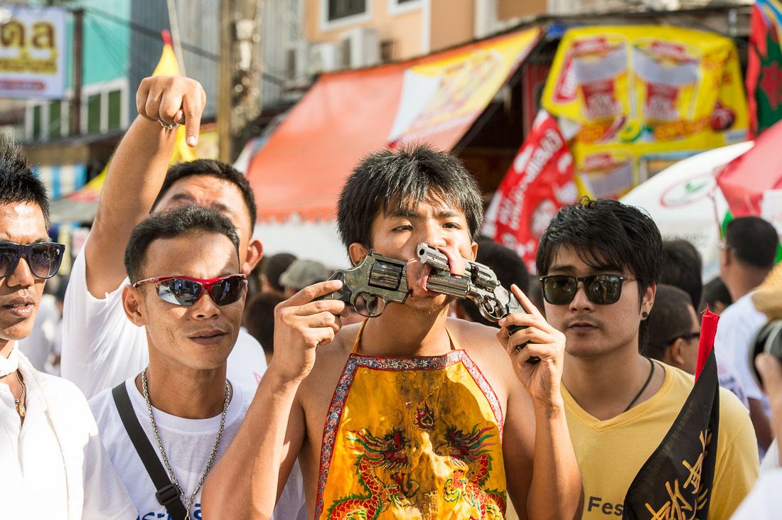 Psychic medium follower of the Bang New Shrine, with two 9mm pistols pierced through his cheecks, taking part in a street procession during the annual Chinese vegetarian festival. Phuket, Kingdom of Thailand, Indochina, South East Asia