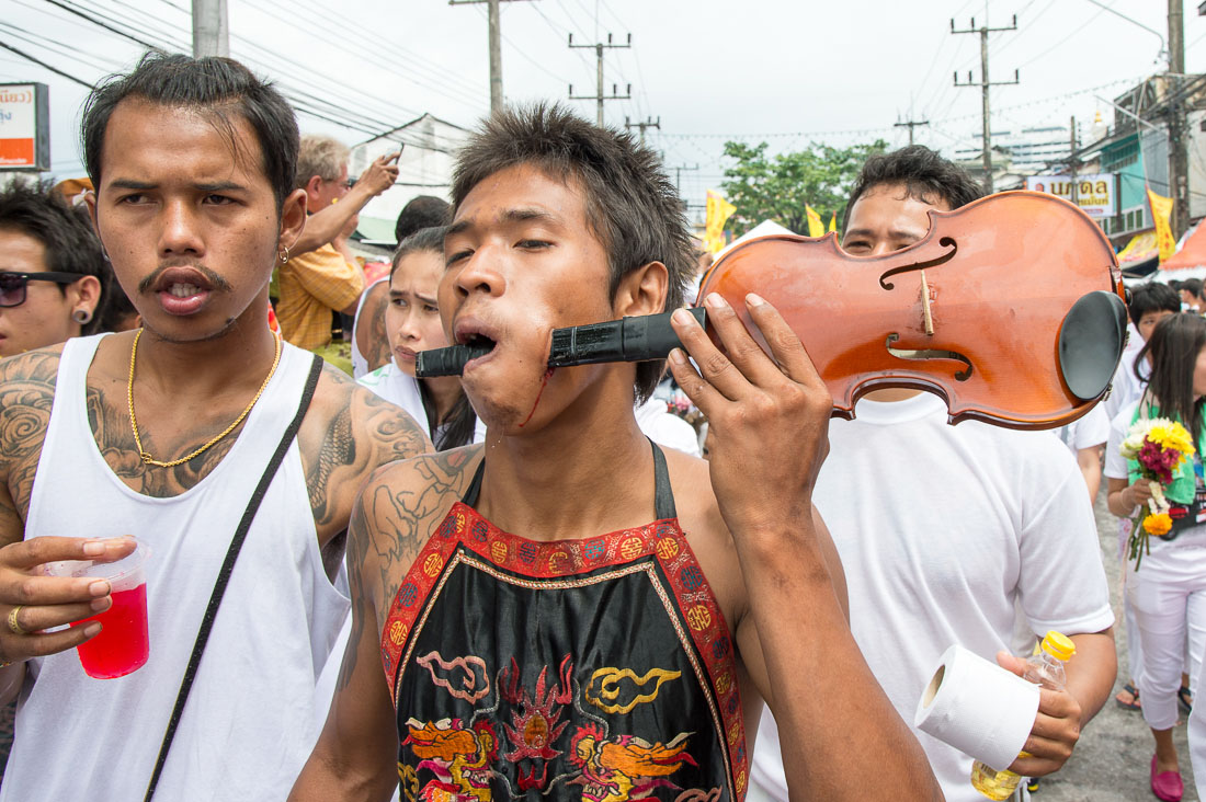 Psychic medium follower of the Bang New Shrine, with a violin neck pierced through his cheeck, taking part in a street procession during the annual Chinese vegetarian festival. Phuket, Kingdom of Thailand, Indochina, South East Asia
