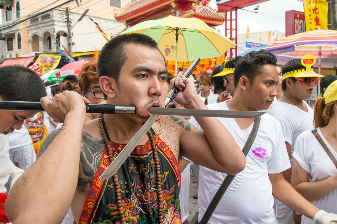 Psychic medium follower of the Bang New Shrine, with two large oriental knives blades pierced through his cheecks, taking part in a street procession during the annual Chinese vegetarian festival. Phuket, Kingdom of Thailand, Indochina, South East Asia