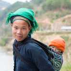A young woman from the Nung people ethnic minority, wearing traditional costume, carrying her baby, Ha Giang province. Viet Nam, Indochina, South East Asia.