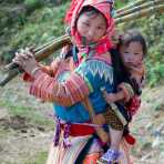 Young mother from the Red Hmong people ethnic minority, carrying her baby, wearing traditional costume, countryside Ha Giang province. Viet Nam, Indochina, South East Asia.