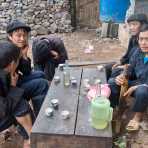 A group of man from the Black Hmong people ethnic minority group, wearing the traditonal berret, having a smoke and few shots of what they call whiskey a spirit distilled from rice. Lung Pin market, Ha Giang province, Viet Nam, Indonesia, South East Asia