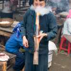Young man from the Black Hmong people ethnic minority group, wearing the traditional costume, taking a strong puff from his bamboo bong. Meo Vac market, Ha Giang province, Viet Nam, Indonesia, South East Asia