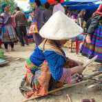 An old woman from the Flower Hmong people ethnic minority wearing the traditional costume and bamboo hat cleaning sugar cane, Bac Ha market, Lao Cai Province, Viet Nam, Indochina, South East Asia