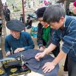 A taylor from the Flower Hmong people ethnic minority group, wearing his traditional beret, working with his Chinese  sewing machine at busy market in Lung Phin, Ha Giang Province, Viet Nam, Indochina, South East Asia